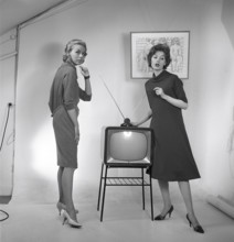 Television in the 1950s. Two young women are standing dressed in a typical 50s dress beside a