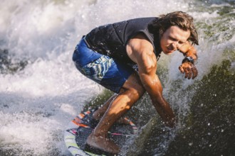 Young athletic man with long hair wakesurfing on waves of river in sunny summer weather. Ttheme