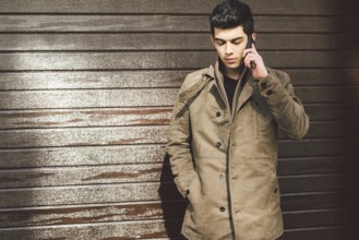 Portrait of a model young mulatto male Turkish Mediterranean race brunet in coat uses hand phone