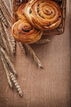 Wicker basket with raisin pastry wheat ears on oaken wooden board food and drink concept