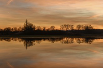 Trees reflecting in the water at sunset. Winter landscape red and orange sky. Bas-Rhin, Alsace,