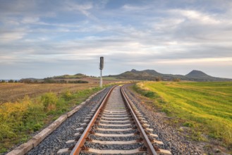 Old Railway tracks running through a field stretch to rural countryside at sunset. Single railway