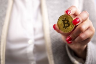 Virtual cryptocurrency money Bitcoin golden coin in the left hand of a woman with red nail polish.