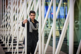 Stylish Young Handsome Man in Black Coat Standing in City Centre Street among White Metal Bars of