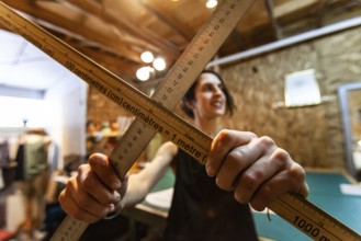 A closeup view of two wood measuring rods being held by a woman tailor inside her retro studio.
