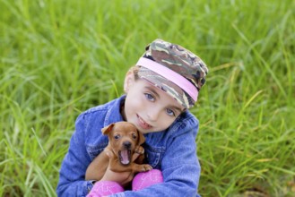 Little girl with pet puppy mascot mini pinscher in outdoor green grass