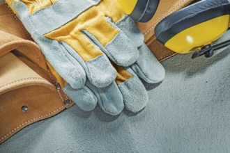 Set of leather tool belt protective gloves earmuffs on concrete background