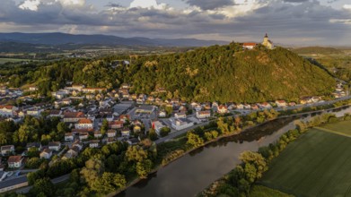 View of a town with a castle on a green hill surrounded by a river in the warm evening light,