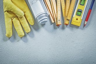Protective gloves construction level wooden meter blueprints pencil on concrete background building