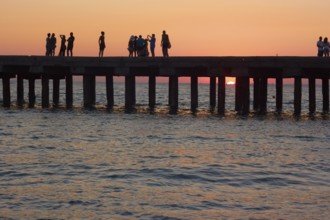 Groups of people on the old pier are photographed and admire the beautiful sunset over the Black