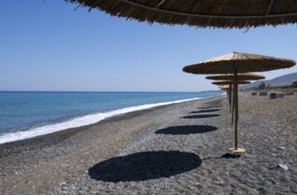 Tropical beach umbrellas providing sunshade for swimmers at an empty beach. Summer vacations.