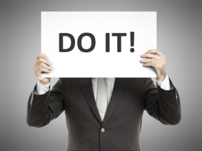 A business man holding a paper in front of his face with the text do it