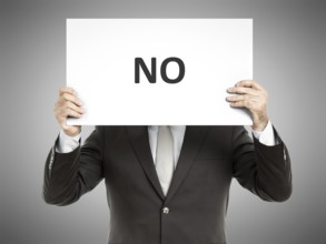 A business man holding a paper in front of his face with the word no