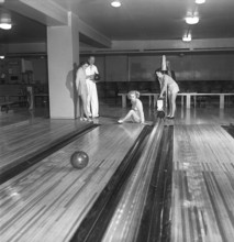 Bowling in the 1950s. A man with three young women in a bowling alley. They are dressed in short