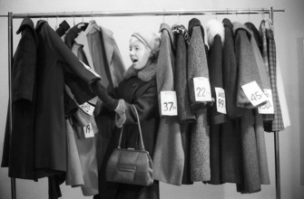 Great discounts of outerwear in the 1960s. A woman stands by a clothes rack, choosing from