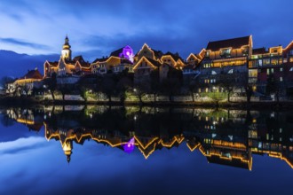 Christmas illuminated house facade of Frohnleiten reflected in the river Mur, blue hour,