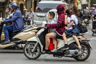 A person with children on a motorbike in a busy city street, woman with children on a scooter in