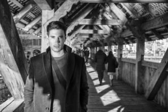 Young dark haired man standing on wooden medieval footbridge in Switzerland while looking away