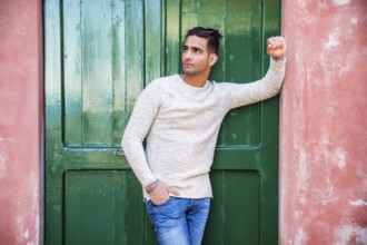 Elegant young man leaning against old wall and green door