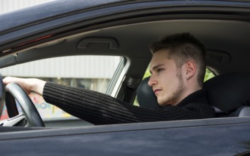 Handsome blond young man sitting in his car, looking in front of him