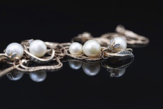 Gold earrings and rings with white pearls lie on a black mirror surface