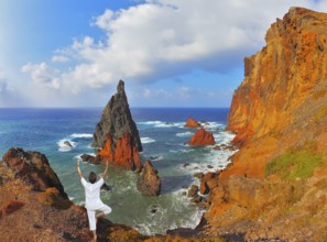 The woman ashore in a white suit for yoga carries out a pose Tree. Atlantic storms. Colorful