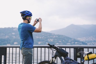 Cyclist taking pictures with smart phone. Caucasian man in bike helmet taking photo of landscape.