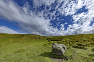 Vast rolling mountain landscape with a cliff and lush green meadows and dramatic skies on the edge