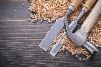 Close up of joiner's hammer and metal firmer chisels in wooden planning chips on vintage wood board