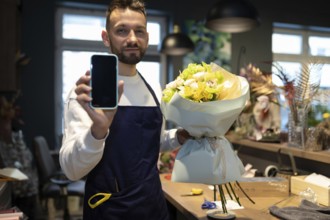Ein florist mit einem strauß in den händen zeigt den bildschirm eines smartphones vor dem