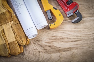 Blueprints protective gloves pipe wrench cutter on wooden board plumbing concept