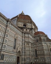 Florence Cathedral with its intricate marble facade and iconic red dome under a cloudy sky.
