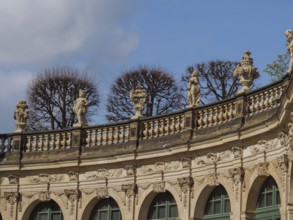 Detailed baroque design of the Zwinger with sculptures and bare trees in front of a blue sky,
