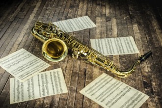Beautiful yellow saxophone and paper with music score notes lying on a vintage wooden stage