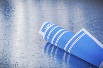 Blue rolled up construction plans on scratched metallic background