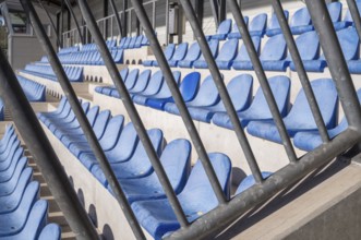 Rows of empty blue plastic stadium seats behind a metal barrier await the return of fans