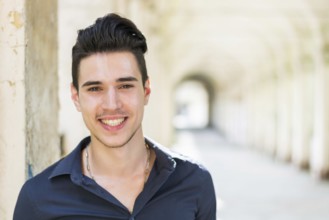 Smiling young man wearing black shirt looking at camera outdoor under arched cloister