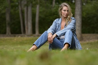 A beautiful blonde model enjoys the late summer sun outdoors. Surrounded by lush greenery and soft