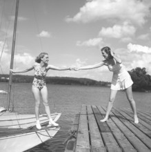 1940s summer. Two young at a marina on a summer's day. The girl getting from the boat onto the