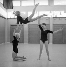 Gymnastics in the 1960s. Three teenage girls are practising gymnastics together in a gymnasium hall