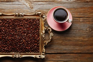 Coffee cup and beans on vintage golden tray in wooden old table