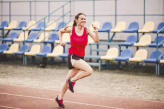 Female runner jogging on stadium track, woman athlete running and working out outdoors, sport and