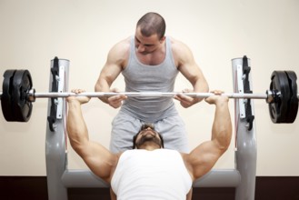 A handsome young muscular sports man doing bench press with a little help