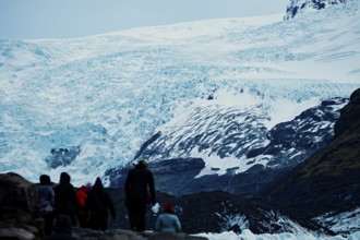Group of tourists walking towards a large glacier under a cloudy sky, iceberg, glacier, snow, ice