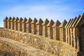 Long stone wall with regular battlements under a blue sky in sunlight, monastery with castle