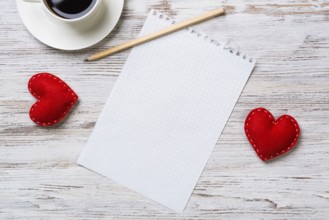 Coffee cup notepad pencil and two red hearts on wooden surface