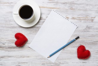 Coffee cup notepad pencil and two red hearts on wooden surface