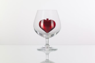 Red heart inside a glass of cognac on a glass plate
