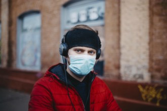 Man with a mask and headphones against a brick wall backdrop