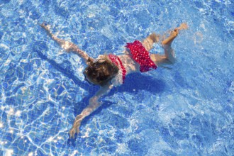 Bikini kid girl swimming on blue tiles pool in summer vacation